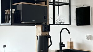 Une cuisine dotée d’un plan de travail en bois, d’un évier noir, d’une machine à café et d’étagères où sont rangés les ustensiles de cuisine et des plantes.