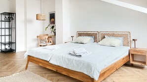 Une chambre avec un lit en bois, une petite table de chevet en bois, un luminaire suspendu, une étagère fixée au mur et une chaise.