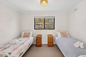 A bedroom with two single beds, a window, a ceiling light, and a small wooden dresser.