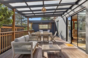 A covered outdoor patio with wooden furniture, a glass door leading to an interior space, and a view of the surrounding area. - Carji (Anglesea)