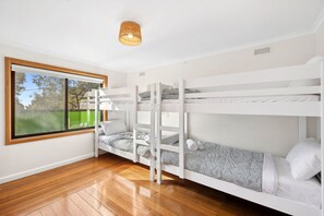 A bunk bed room with a window, wooden flooring, and a hanging light fixture. - Carji (Anglesea)