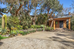 A modern house with a stone pathway leading to the entrance, surrounded by various plants and trees. - Carji (Anglesea)