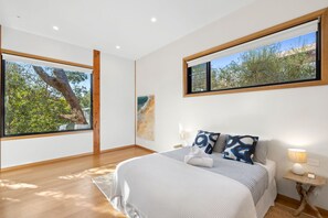 A bedroom with a large bed, a nightstand, a lamp, and a painting on the wall. - Carji (Anglesea)