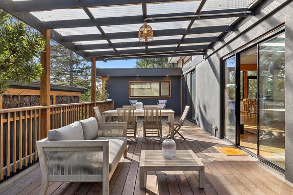 A covered outdoor patio with wooden furniture, a glass door leading to an interior space, and a view of the surrounding area. - Carji (Anglesea)