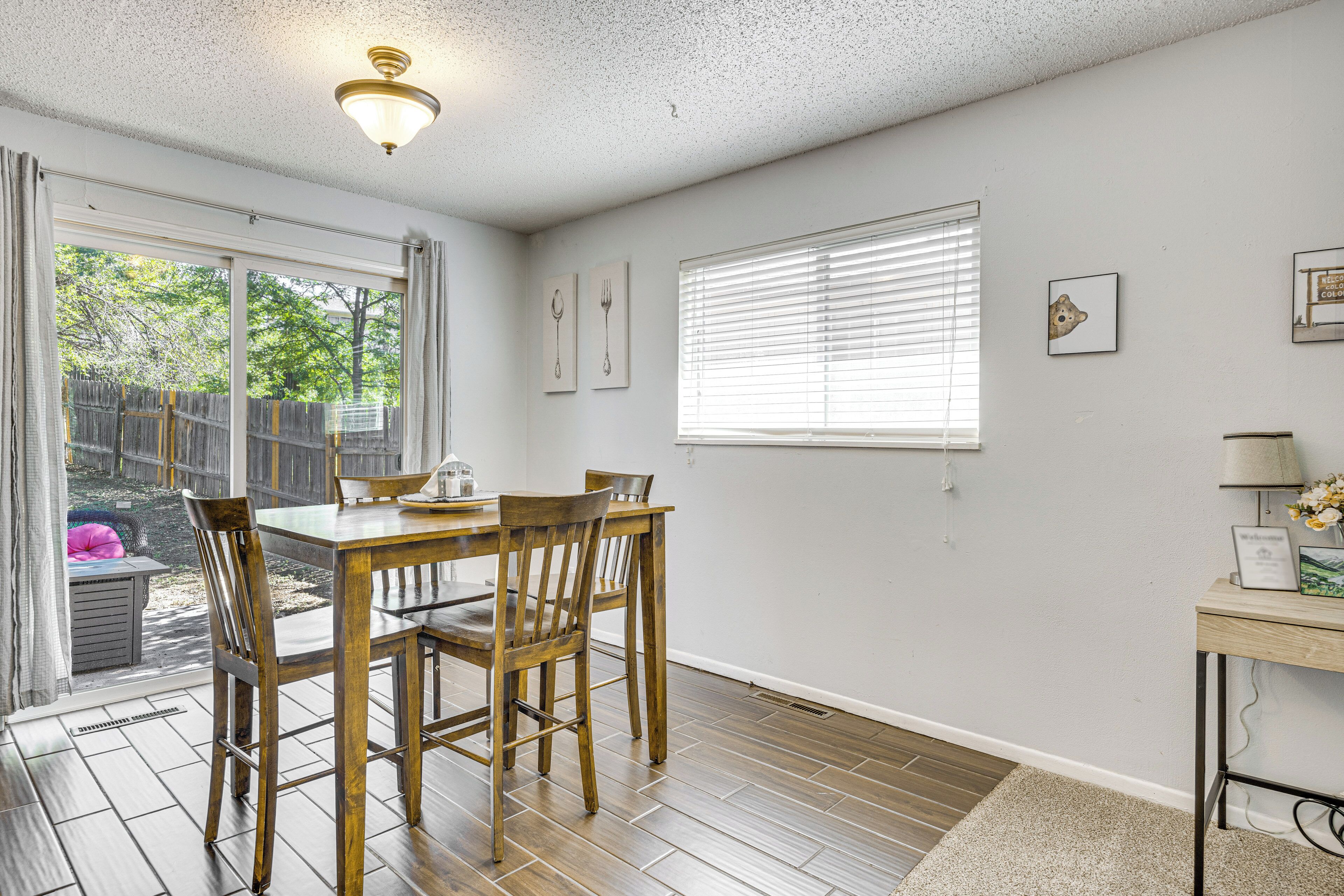 A dining area with a wooden table and chairs, a window with blinds, and a wall with framed pictures.