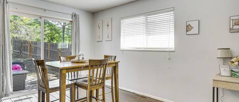 A dining area with a wooden table and chairs, a window with blinds, and a wall with framed pictures.