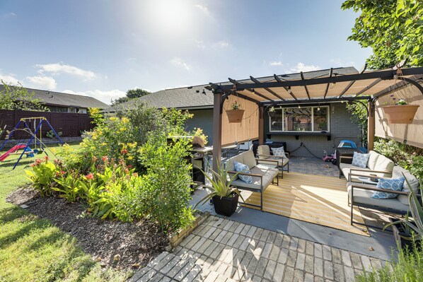 A covered patio area with outdoor furniture, a swing set, and potted plants. - Outdoor Pool & Fire Pit: Modern Austin Home (Austin)