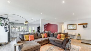 A modern living room with a sectional sofa, a patterned rug, and a kitchen in the background.