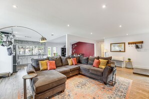 A modern living room with a sectional sofa, a patterned rug, and a kitchen in the background.
