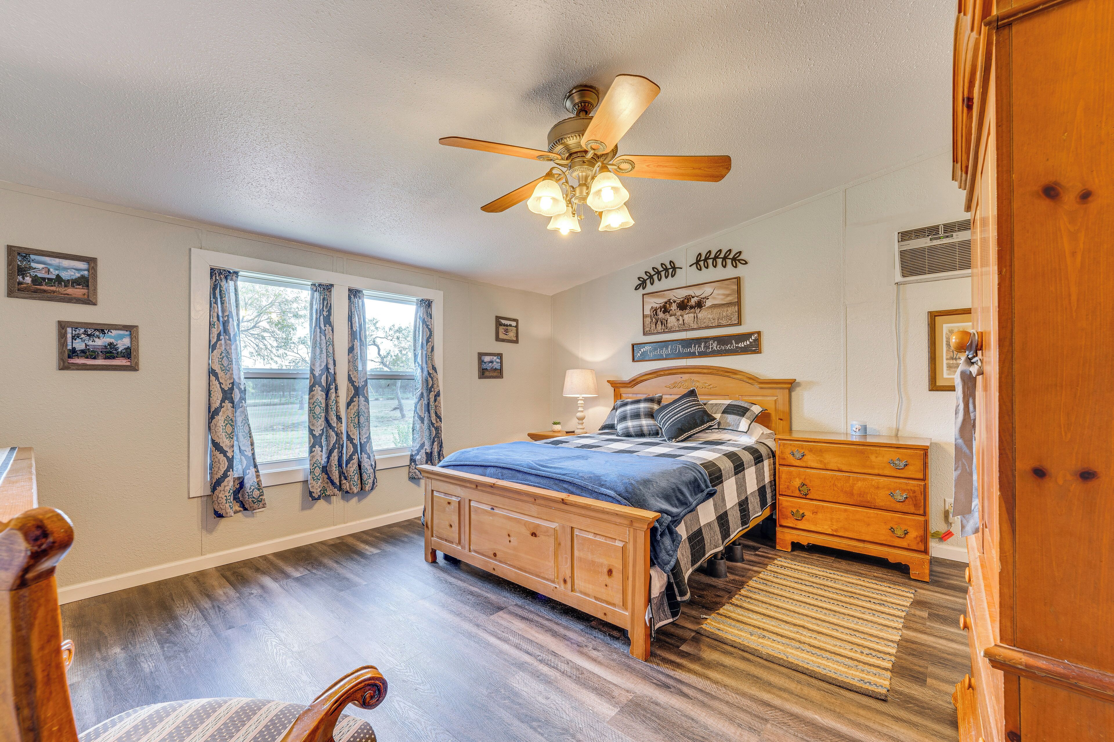 A bedroom with a wooden bed, a nightstand, a dresser, a ceiling fan, and a window with curtains.