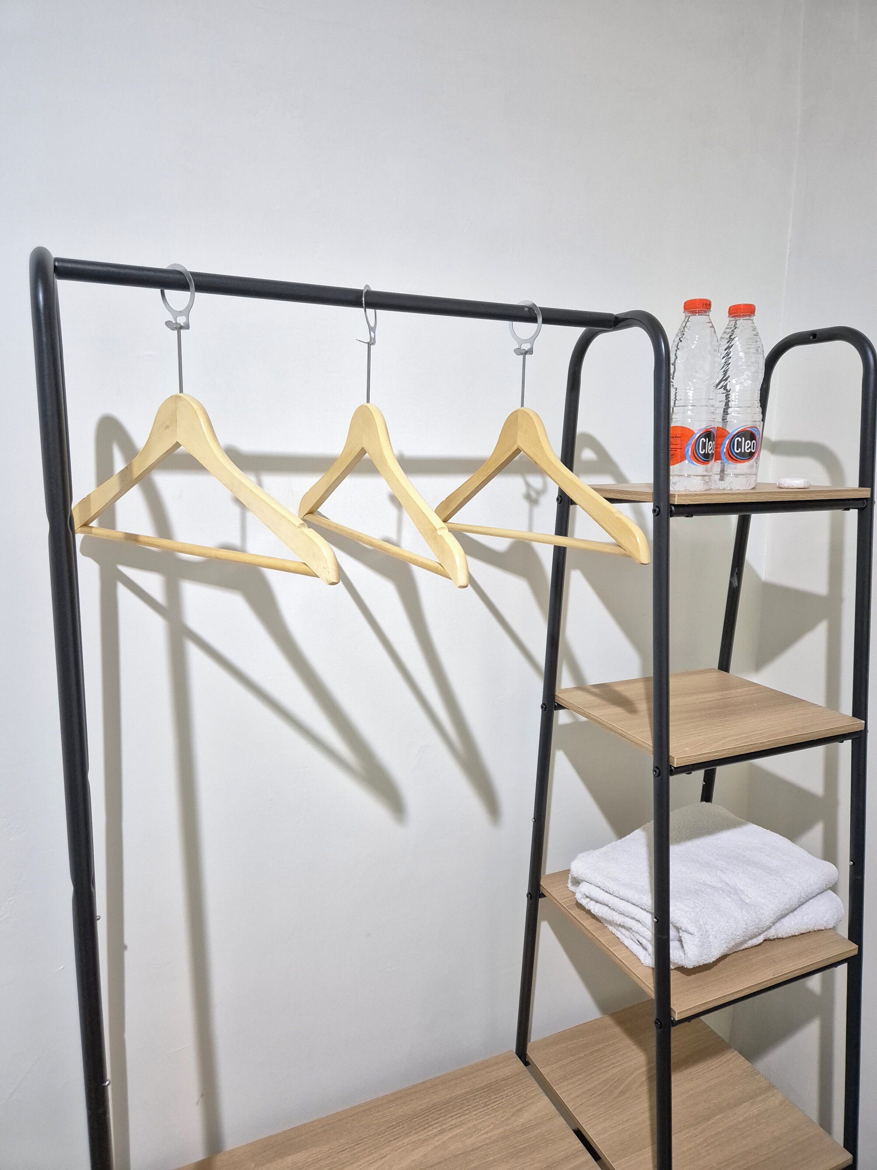 A metal rack with wooden hangers and shelves, holding folded towels and two bottles of water.