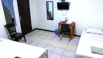 A room with a bed, a desk with a chair, a television mounted on the wall, and a window with curtains.