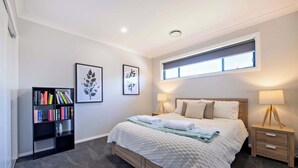 A bedroom with a bed, bedside tables, a bookshelf, and framed artwork on the wall.