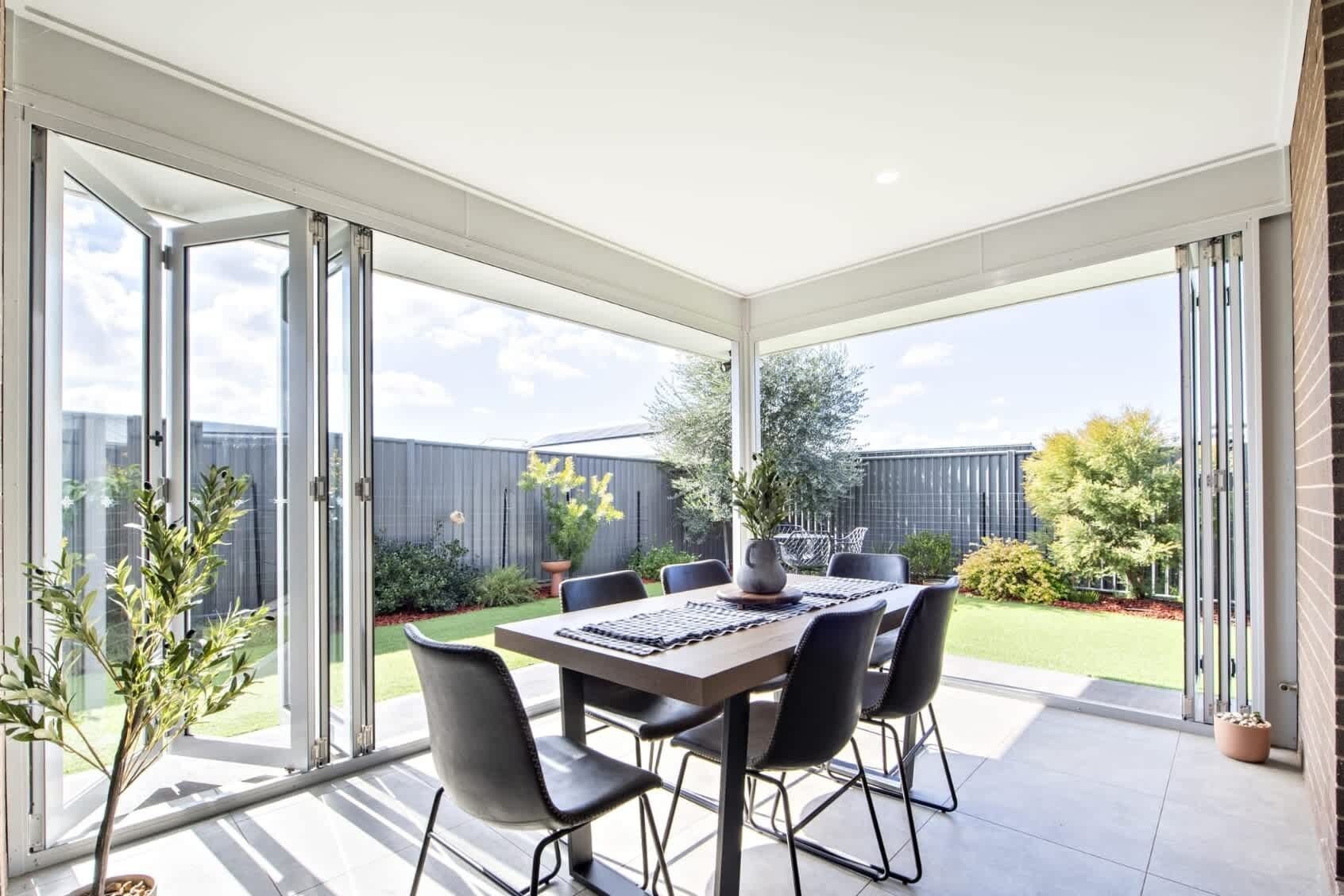 A covered patio with a table and chairs, a potted plant, and a view of a fenced backyard.