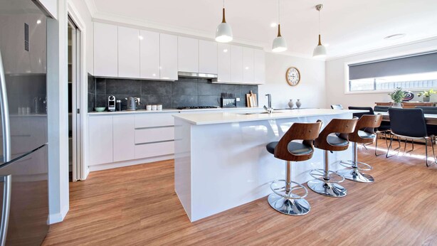 A modern kitchen with white cabinets, a central island with bar stools, stainless steel appliances, and pendant lighting.