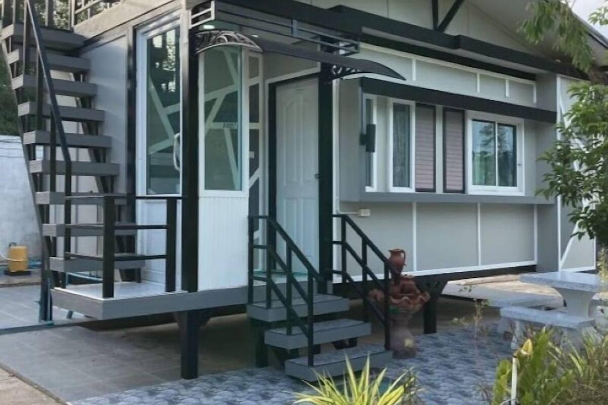 A modern house with a staircase leading to a balcony, a small porch area, and a garden with potted plants.