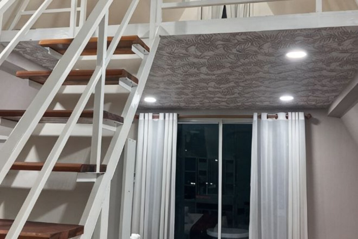 A staircase with wooden steps and white railings, a ceiling with a textured pattern, and a window with white curtains.