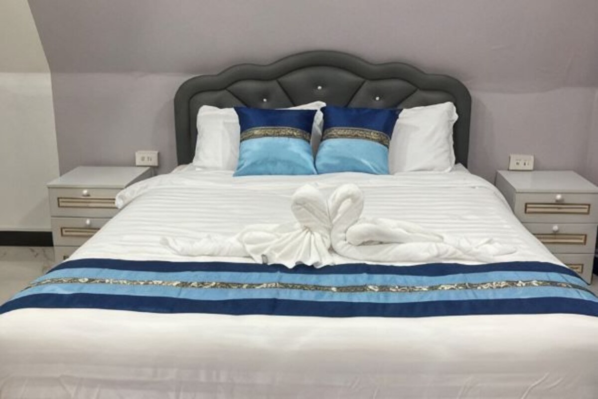A neatly made bed with a headboard, two bedside tables, and a decorative towel arrangement.