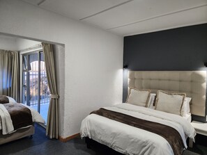 A hotel room with a large bed, a separate chair, a view through a glass door, and a dark accent wall. - Busa House Self Catering Guest house (White River)