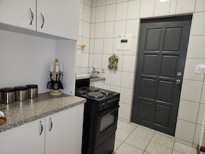 Una cucina con mobili bianchi, un piano cottura nero e una porta nera.