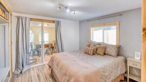 A bedroom with a large bed, a sliding glass door leading to a balcony, and a bedside table with a lamp. - #StayinMyDistrict Lakeside Cottage (Lakeside)