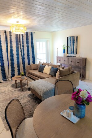 A living room with a sofa, coffee table, dining table, and a chandelier.