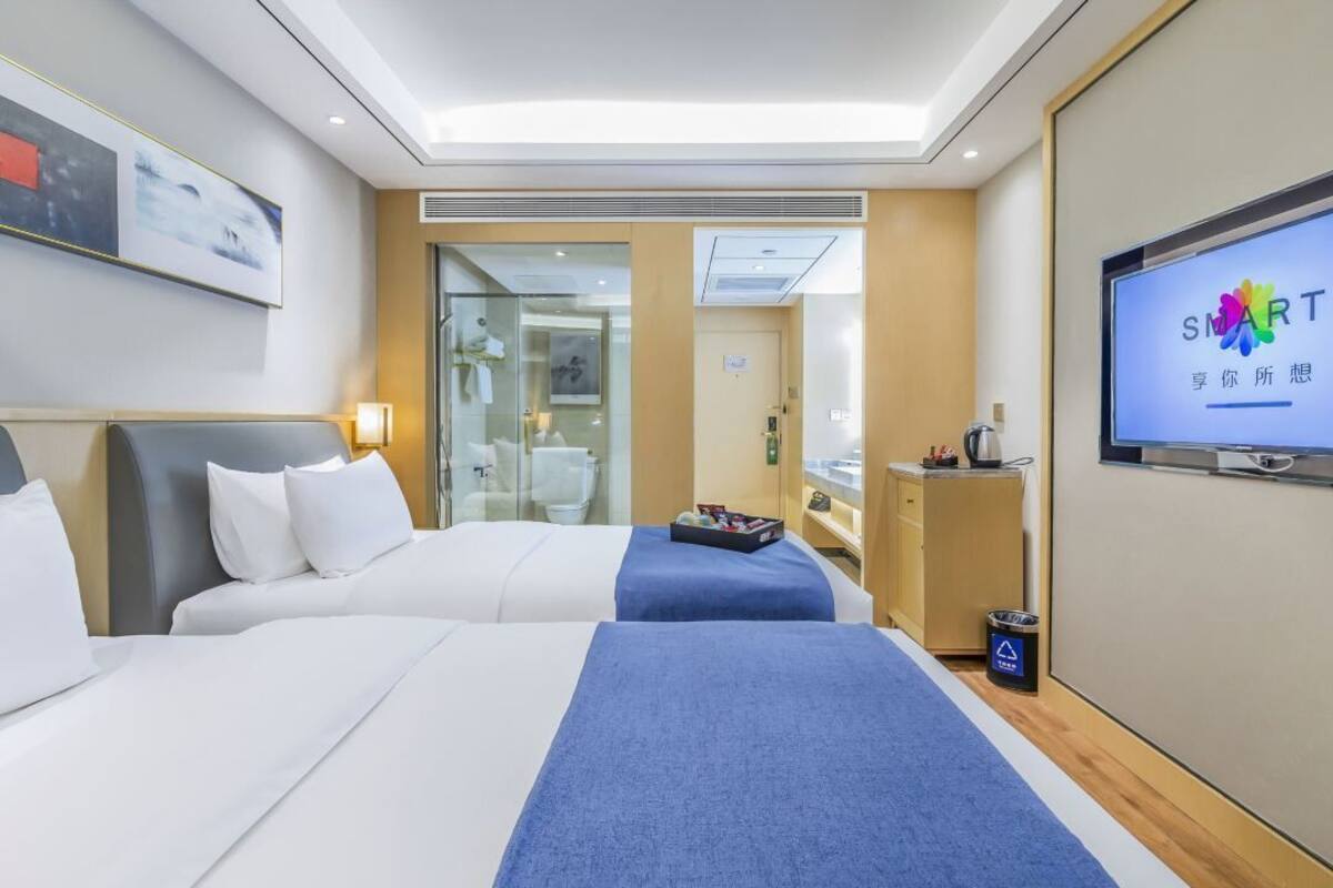 Een hotelkamer met twee bedden, een televisie, een bureau en een badkamer zichtbaar door een glazen deur.