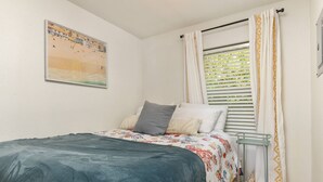 A bedroom with a bed, a window with blinds, a painting on the wall, and a small table. - 2 Blocks From Beach, Unit #6, Pet Friendly, Great Location, WiFi, Kitchen (Rockaway Beach)