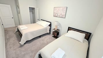 A bedroom with two beds, a bedside table with a lamp, and a door leading to a closet.