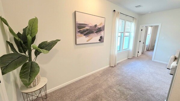 A hallway with a large potted plant, a framed abstract painting, and a carpeted floor.