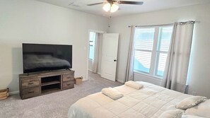 A bedroom with a bed, a television on a wooden stand, a ceiling fan, and a door leading to another room. - Tiger Tracks Townhome Stay in Baton Rouge - BC1009 (Baton Rouge)