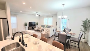 A modern living room with a sofa, coffee table, and a TV. There's a dining area with a table set for four. - Tiger Tracks Townhome Stay in Baton Rouge - BC1009 (Baton Rouge)