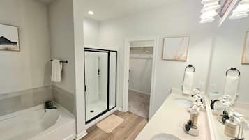 A bathroom with a bathtub, a glass-enclosed shower, a vanity with a mirror, and a towel rack.