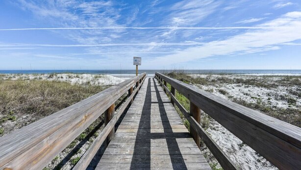 A wooden boardwalk leading to a beach with a clear sky.