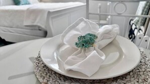 A white plate with a decorative item on a table, a bed, and a white chair in the background.