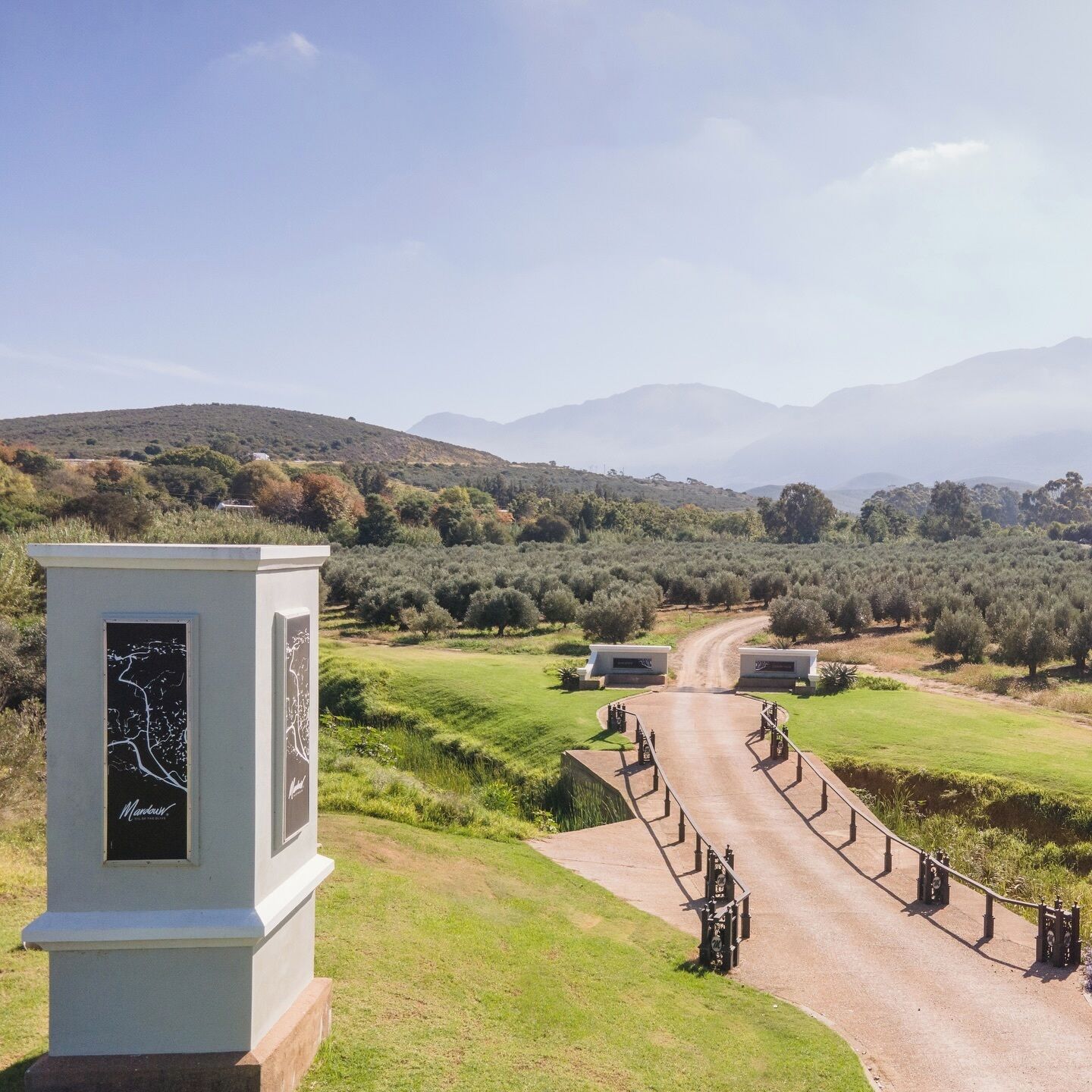 A rural landscape with a paved road leading to a white building with a map display.