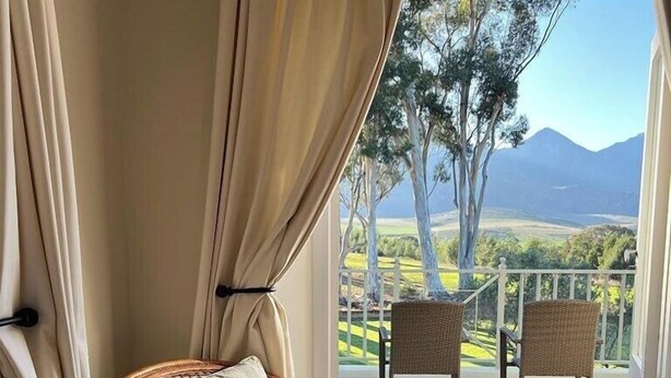 Ein Balkon mit Korbstühlen, Blick auf eine Berglandschaft und einem weißen Geländer.