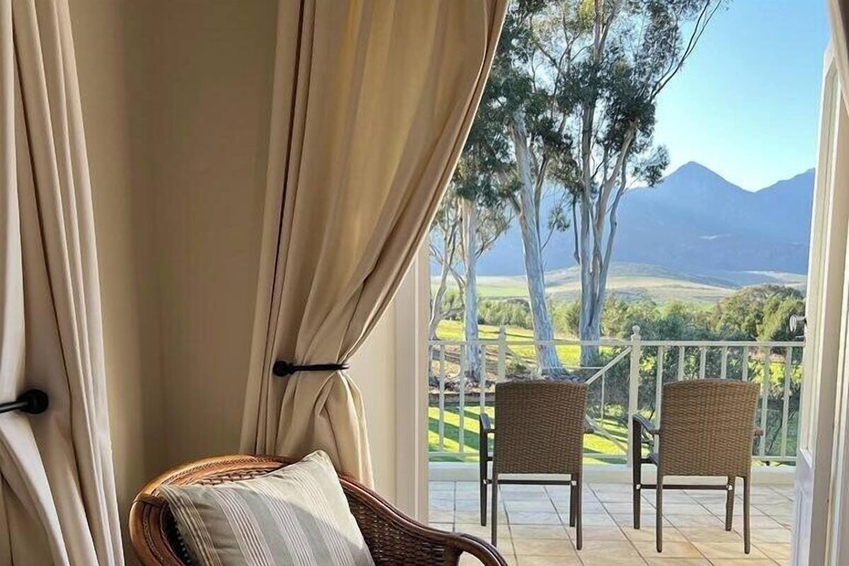 Een balkon met rieten stoelen, uitzicht op een bergachtig landschap en een witte balustrade.