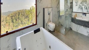 A bathroom with a bathtub, toilet, and sink, featuring marble walls and a large window with a view of a forest. - Mount Pico (Yercaud)