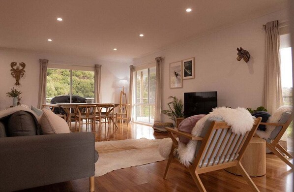 A living room with a sofa, a TV, a dining table, and chairs. - Redbill Surf Shack - SO Close to Redbill Beach! (Glamorgan-Spring Bay)