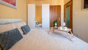 Ein Schlafzimmer mit einem Bett, Kissen, einem Nachttisch mit Tassen und einer Pflanze, einem Kleiderschrank und einer Tür mit grünem Hintergrund.