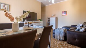Ein modernes Wohnzimmer mit einer Couch, einem Esstisch mit Stühlen, einem Fernseher und einem kleinen Schrank.