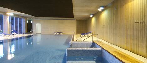 An indoor swimming pool with tiled walls, a wooden deck, and lounge chairs.