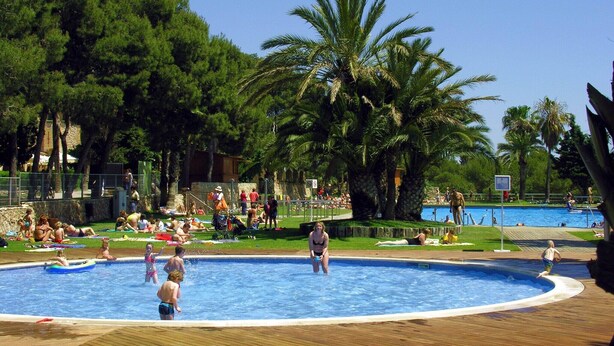 A swimming pool area with multiple pools, palm trees, and people relaxing and swimming. - Chalet with air conditioning on beautiful park (Barcelona)