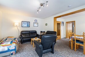 Un salon meublé comprenant un canapé, un fauteuil, une petite table et une table à manger avec des chaises.