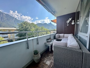 Ein Balkon mit einem Rattan-Sofa, einem kleinen Tisch und einem Blumentopf.