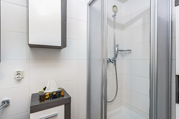 Une salle de bain moderne avec des carreaux blancs, une douche à parois de verre, un miroir et un porte-serviettes.