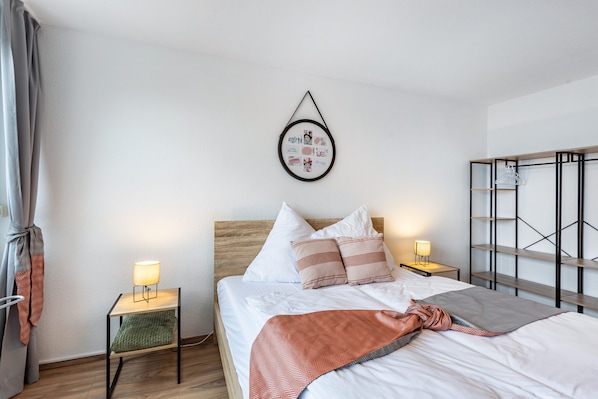 Ein ordentlich eingerichtetes Schlafzimmer mit Bett, Nachttischen, einem Wandbild und einem Kleiderschrank.