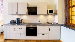 Une cuisine compacte avec des meubles blancs, un four encastré, un four à micro-ondes, une machine à café et un évier.