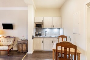 A compact kitchen with a microwave, sink, and cabinets. There is a dining table with chairs and a small cabinet with a TV on the wall.